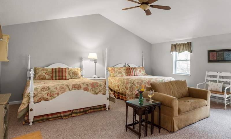 Suite Divine with king bed, queen bed, sofa sleeper. sleeps 5. Spacious bedroom with king and queen beds, a sitting area with twin sofa sleeper. Furnishings are farmhouse cottage with whitewashed furniture.